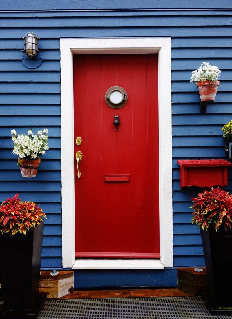 Bright red door in the middle of a white frame surrounded by deep lavender purple siding for a piece on red door ideas