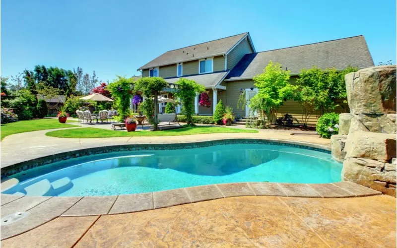 To illustrate what an inground pool costs, a gorgeously-landscaped home with a stamped concrete pool deck overlooks an inground pool