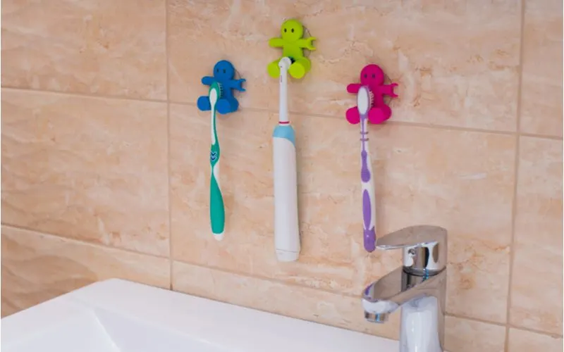 A small bathroom storage idea for those with limited counterspace featuring small suction cup hooks for tooth brushes in the shape of people