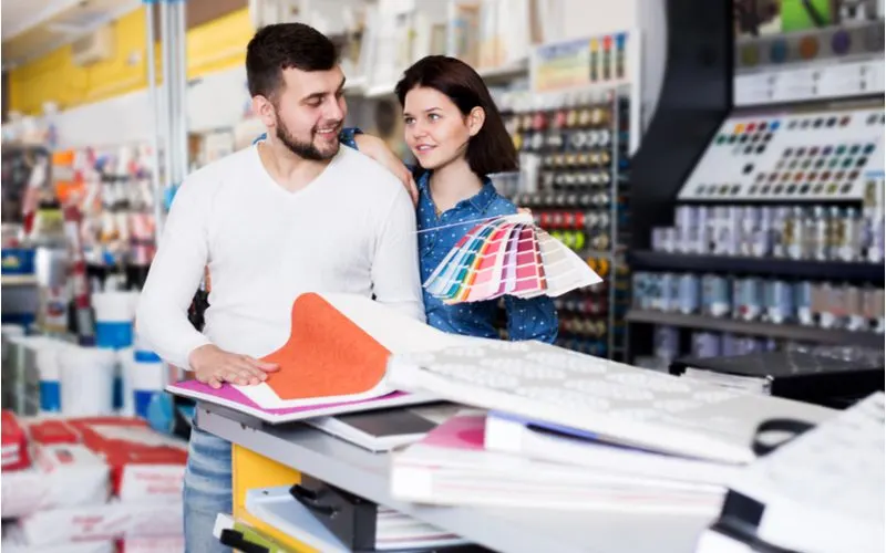 Couple deciding how much paint they'll need to buy by laying out a white paper blueprint on the counter of a home improvement store while holding a paint swatch