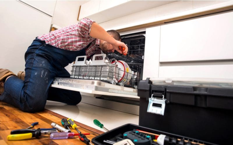 Handyman repairing a dishwasher that won't drain by pulling off the trim pieces and checking the pump motor and air gap