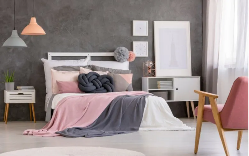 Pink and grey bedroom idea with a simple white bed and a somewhat contemporary aesthetic with pastel hanging lights and a pink upholstered chair with natural wooden legs and white picture frames