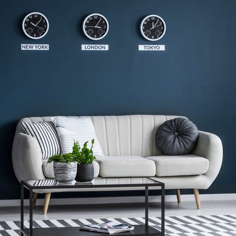 Wall decor above couch ideas featuring stainless steel world clocks mounted on a blue wall above a cream couch
