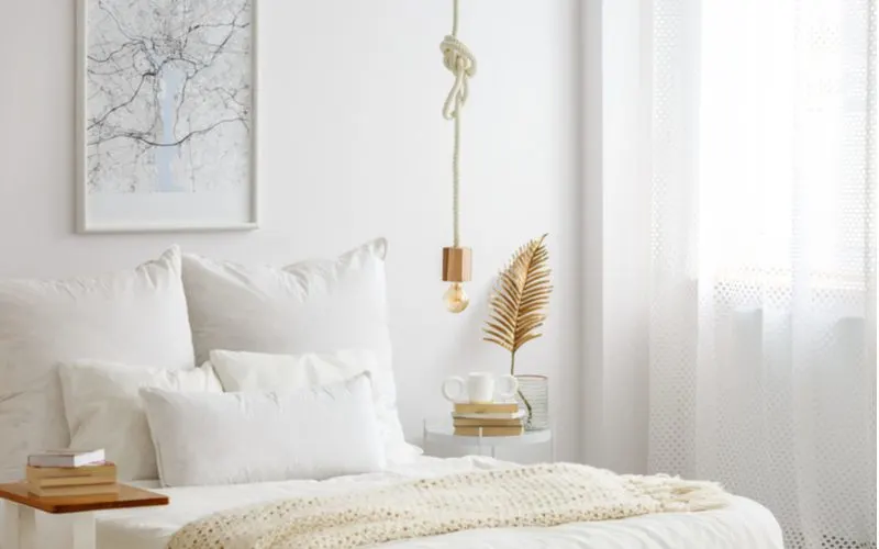 Scandinavian bedroom aesthetic idea featuring a simple white room with light cold and natural wood accents on and around the bed