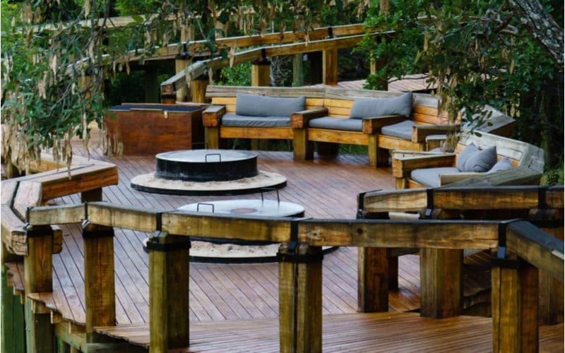 Idea for a fire pit with a big metal wood burning pit above a wooden deck with wooden benches with foam cushions