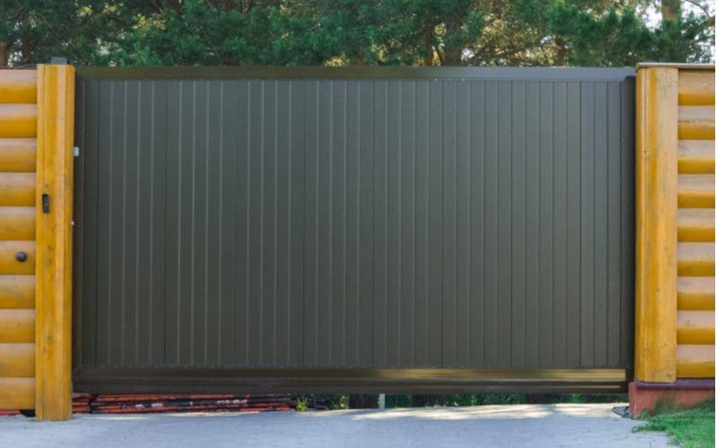 Brown metal driveway gate idea with vertical slats between a log cabin style fence
