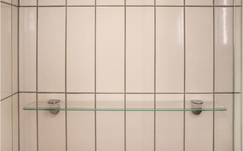 Glass shelf mounted to the wall of a vertically-placed subway tile shower surround as an idea for small bathroom storage