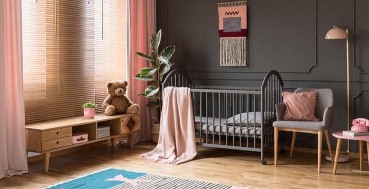 Image for a piece on what color curtains with gray walls featuring a dark gray wainscoted wall in a baby nursery with light pink curtains