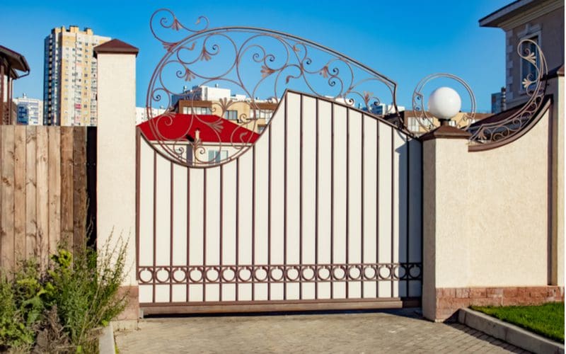 Asymmetrical rounded ornamental gate in an ornate style with wooden slats running vertically for an idea for driveway gates