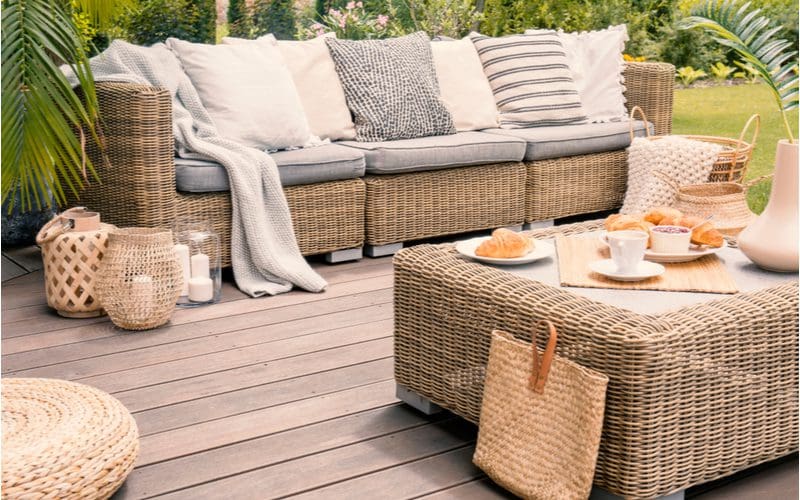 Wicker patio furniture sitting on a light grey wooden deck with new foam cushion replacements just added to the set to change the look