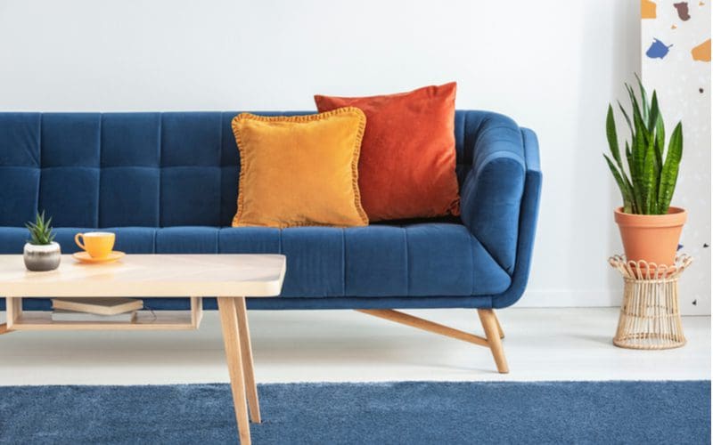 Blue couch living room ideas with a blue couch on which sit red and yellow pillows with a natural wood legged coffee table with a white top