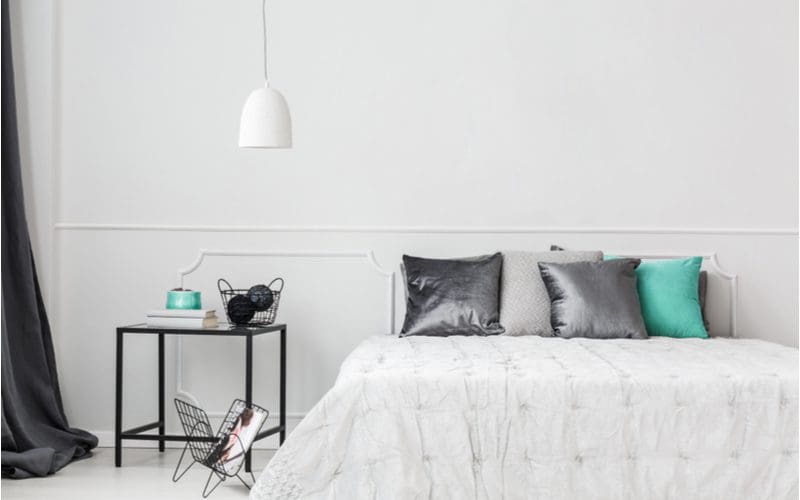 Teal bedroom décor ideas featuring teal and metallic purple pillows with white bedding and an off-white wall with shelf molding