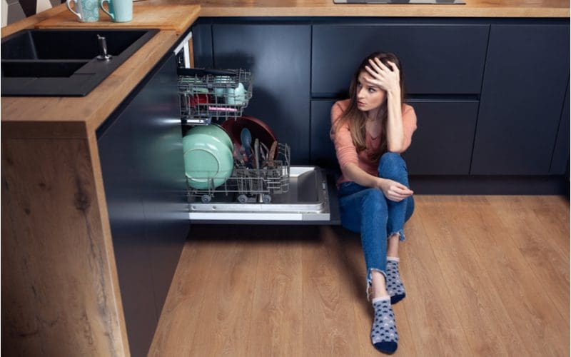 Frustrated woman stressed out and holding her head with her left hand because her dishwasher won't drain