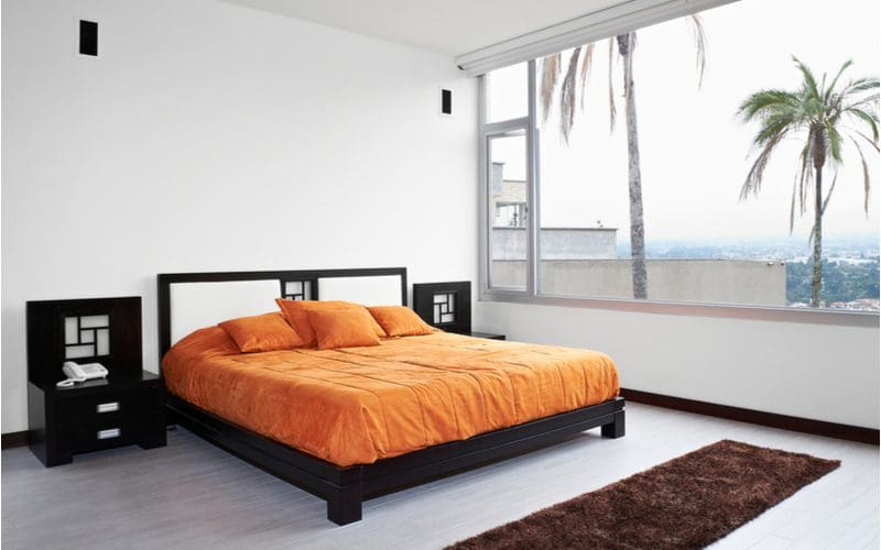 Masculine bedding idea with a black bed with grey flooring and an orange comforter with minimal decorations in the room