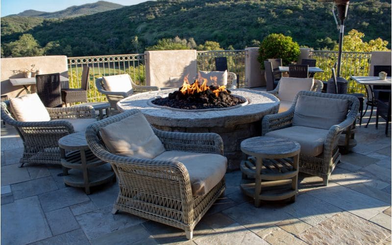 Fire pit idea made of stone with a round concrete topper next to wicker chairs in the middle of a multi-sized paver patio