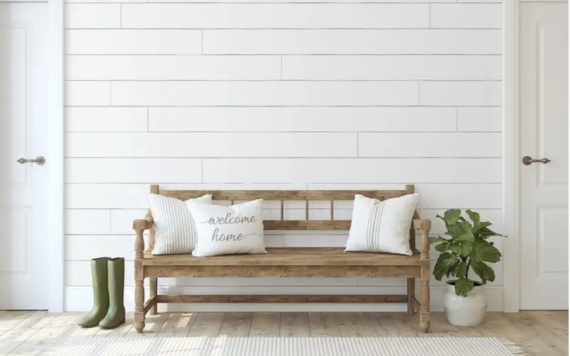 For a piece on farmhouse decor ideas, a rustic unfinished natural wood bench sits in the entryway to a modern home
