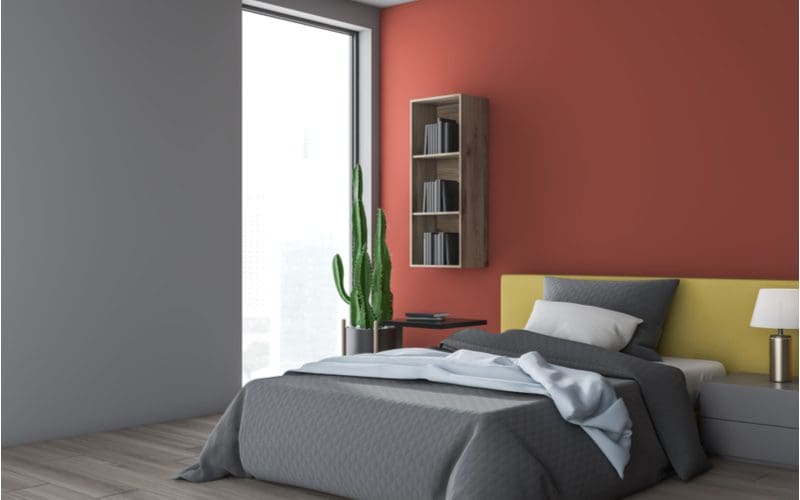 Grey and rust red painted bedroom idea with grey bedding and grey shelving with a bright yellow headboard