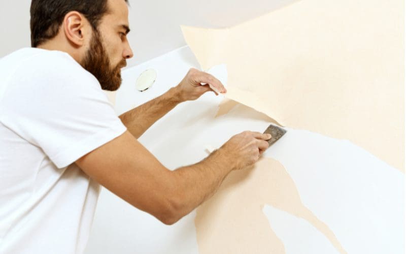 Man installing a peel and stick wall mural (a cheap way to cover a wall) with his hands and a putty knife