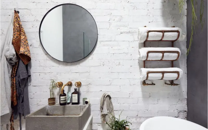 Small bathroom storage idea with rolled towels on curved shelves screwed into a white painted brick wall