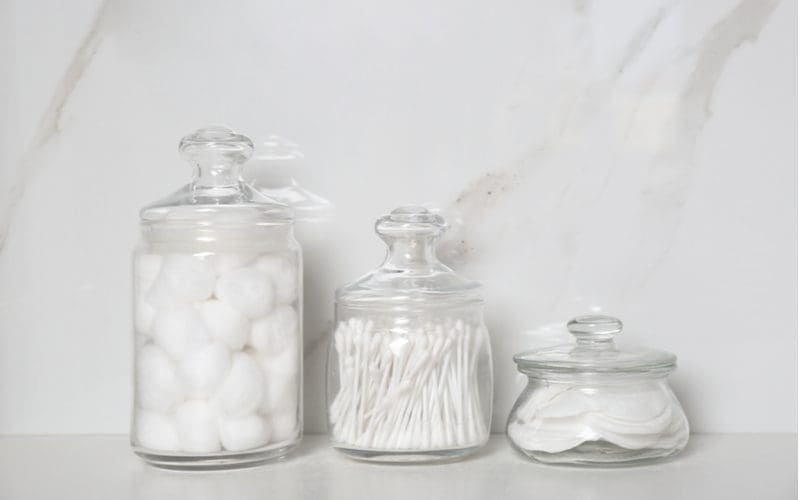 Cotton balls, swabs, and patches inside glass containers for a piece on small bathroom storage ideas