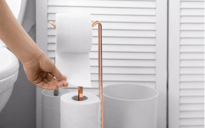 Toilet paper on a golden metal holder being pulled by a person whose face and body are out of frame