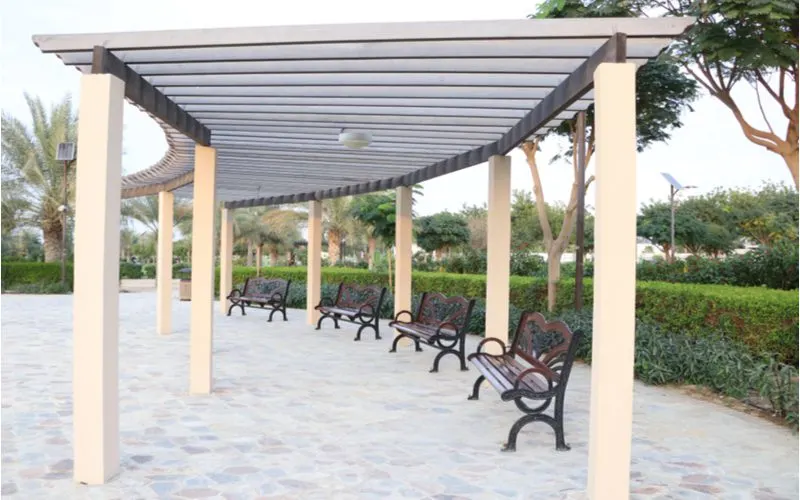 Curved pergola idea with wooden slats running across the top and metal square supports above a stone walkway