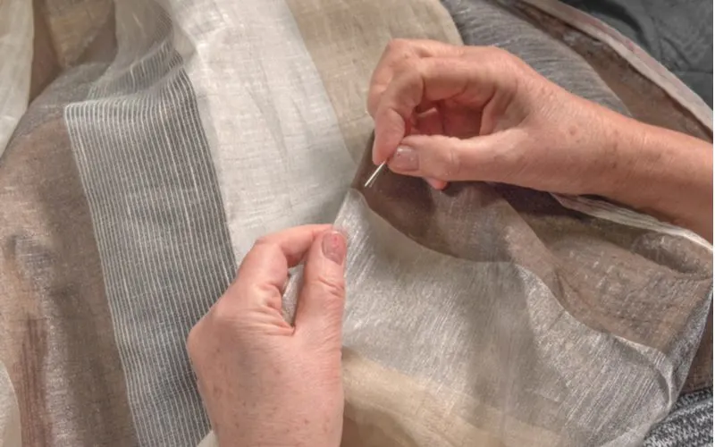 Elderly woman sewing curtains for travers rods at home with sheer and blackout material
