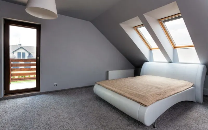 As an image for a piece no grey bedroom ideas, a modern looking white bed sits below a slanted grey wall with windows in the ceiling
