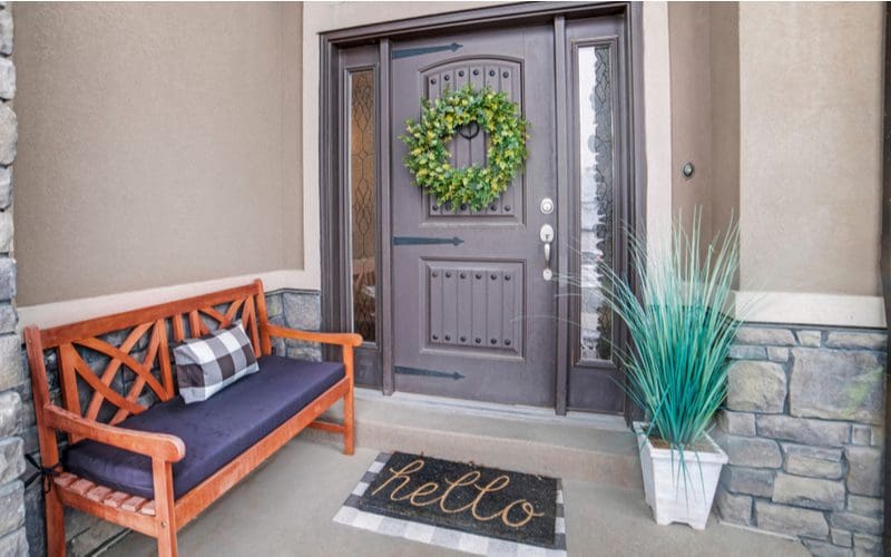 Dark gray front door and trim on a light gray house with stone trim and a bench on the front porch
