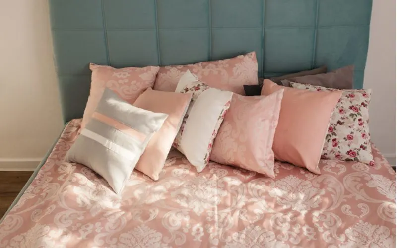 Various colored pillows sitting on a silk pink bedsheet for a piece on dorm room ideas