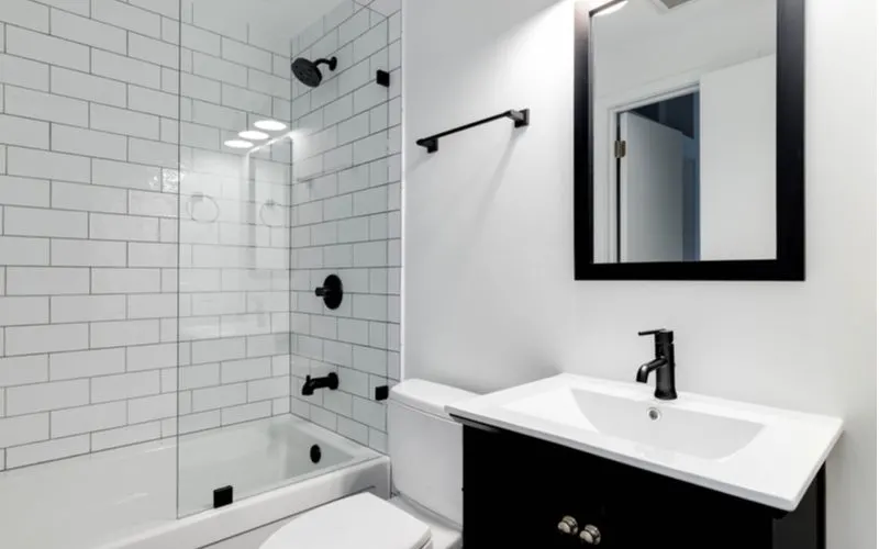 White walled shower with dark fixtures and a dark vanity for a piece on parts of a shower