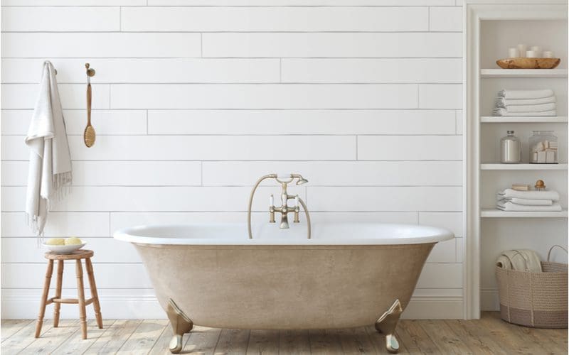 Bathroom full of farmhouse decor with a white shiplap wall, a light brown barnwood floor, and white shelves and wooden fixtures