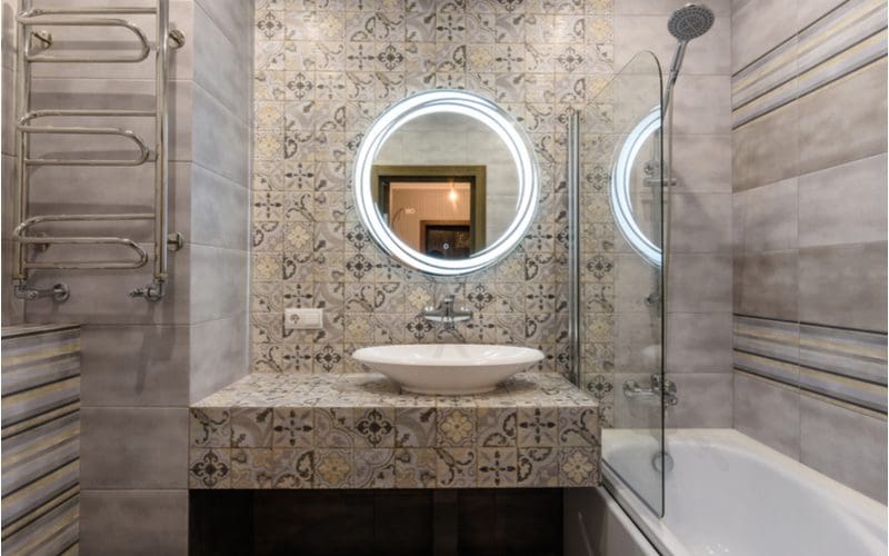 Large patterned wall tile next to a shower in a very small bathroom with a lighted mirror
