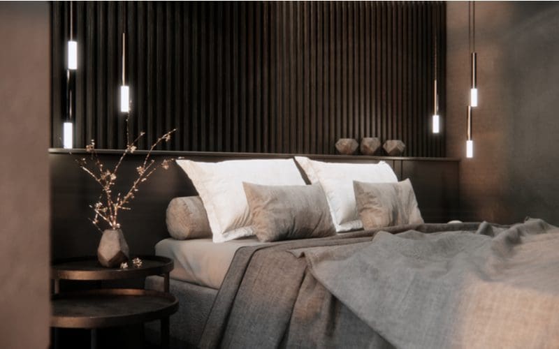 Hanging pendant lights on either side of a modern grey bed above the end tables on which sit unique decorations