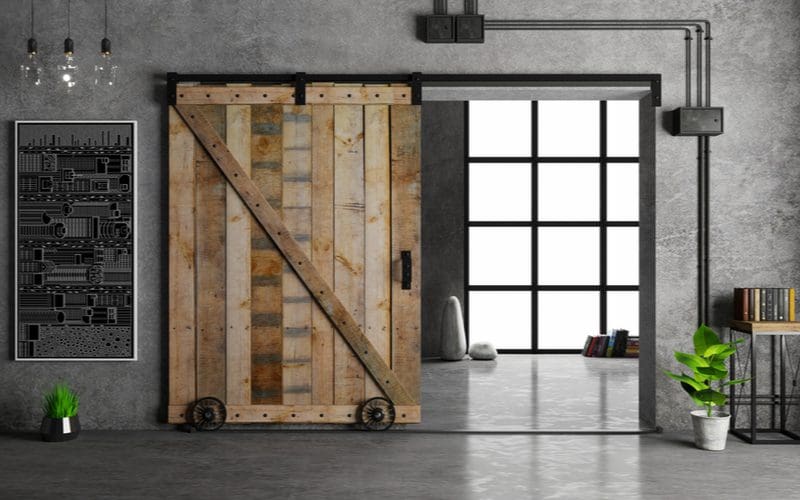 Example of a mens bedroom idea with concrete walls and dark-colored exposed conduit running above a very wide natural wood barn door