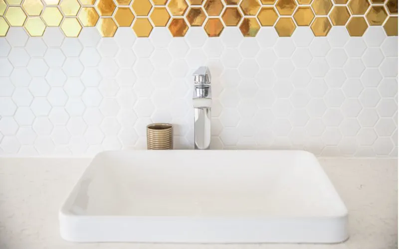 For a piece on white and gold bathroom ideas, a simple white countertop with a white sink bowl and single handle chrome faucet with white and gold hex tiles