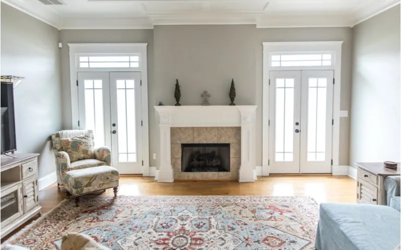Clean and neutral fireplace tile idea featuring a small wood burning fireplace surrounded by grey 12x12 ceramic tile framed by an ornate white mantle