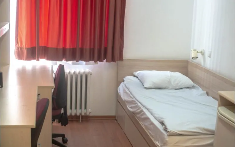 A college dorm room idea featuring a plain white room with a bright red blackout curtain