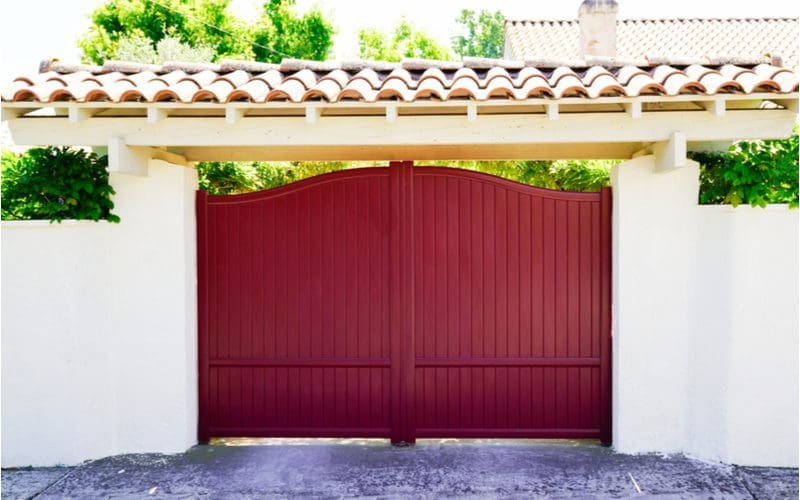 Red wooden driveway gate inspiration between two stucco walls below a slanted terra cotta roof