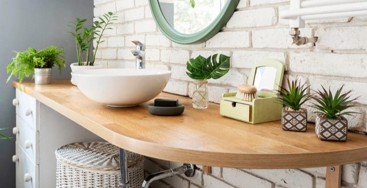 For a piece on bathroom counter decorations, a natural light wooden shelf sits mounted to a brick wall with a bunch of décor on it