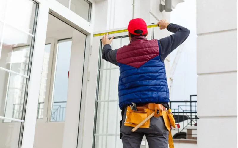 Guy in a blue and red puffy vest measuring a door for a piece on does board and batten siding come in vinyl