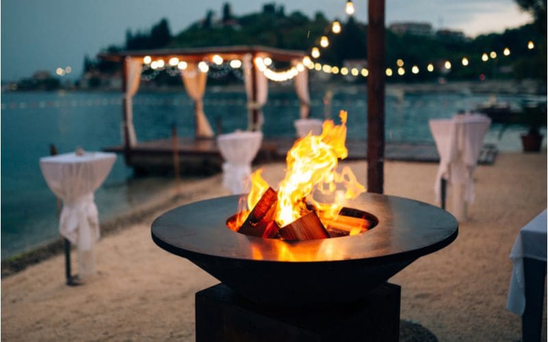 For a piece on fire pit ideas, a modern metal fire pit in the shape of a half-saucer sits in the middle of a beach