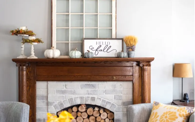 Piece on farmhouse décor ideas showing a dark wooden mantle with bright and airy decorations, white painted pumpkins, and an off-white painted window used as a decoration