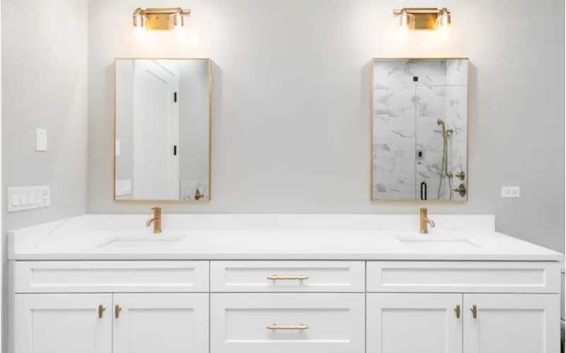 Luxurious white bathroom with white walls and white marble vanity top with gold lights, mirrors, fixtures, and pulls