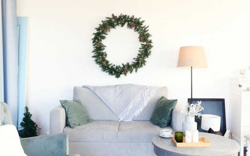 For an example of holiday wall decor above the couch ideas, a spruce wreath hangs on an otherwise drab white wall above a loveseat