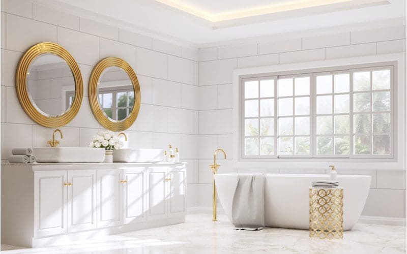 White and gold bathroom ideas featuring a huge expansive bathroom with a standalone tub and gold fixtures and gold mirrors with white tiles on the wall