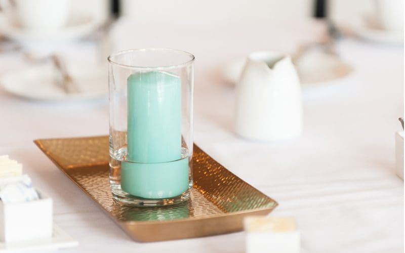 For a piece on teal bedroom decoration ideas, a teal candle sits on a gold decoration holder on a white table