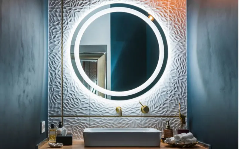 New age modern white and gold bathroom idea with a big round mirror mounted on a white hammered look tile with gold fixtures and decorations