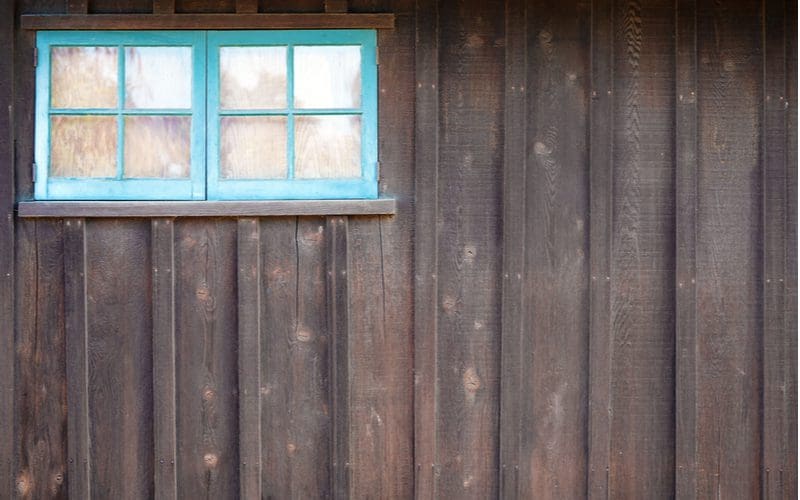 Teal painted wooden window frame on a vertical paneled house side