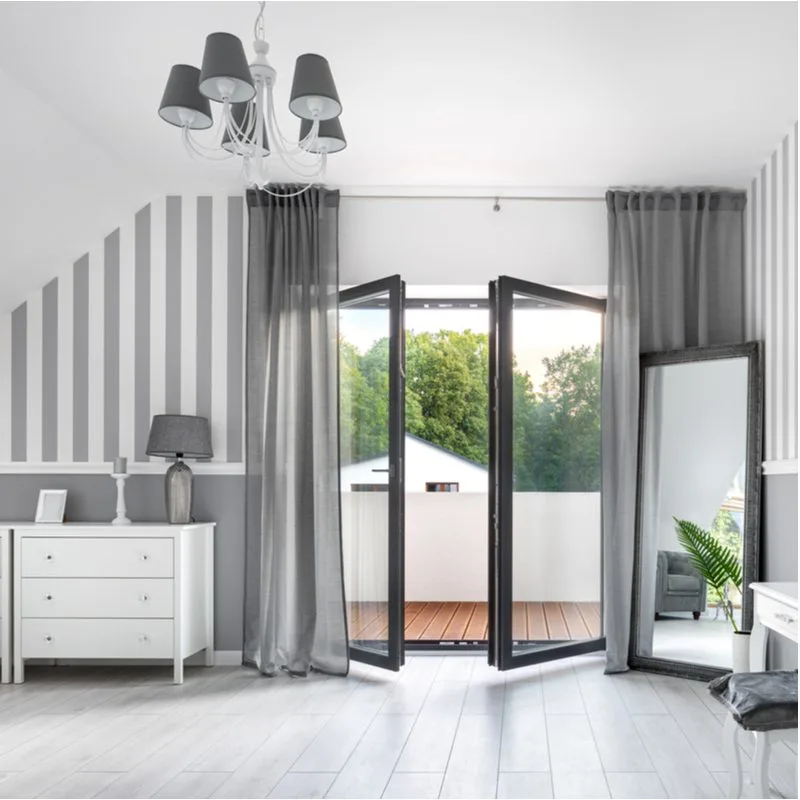 Grey bedroom idea with white and grey vertical striped walls on the sides of big metal glass-lined French doors